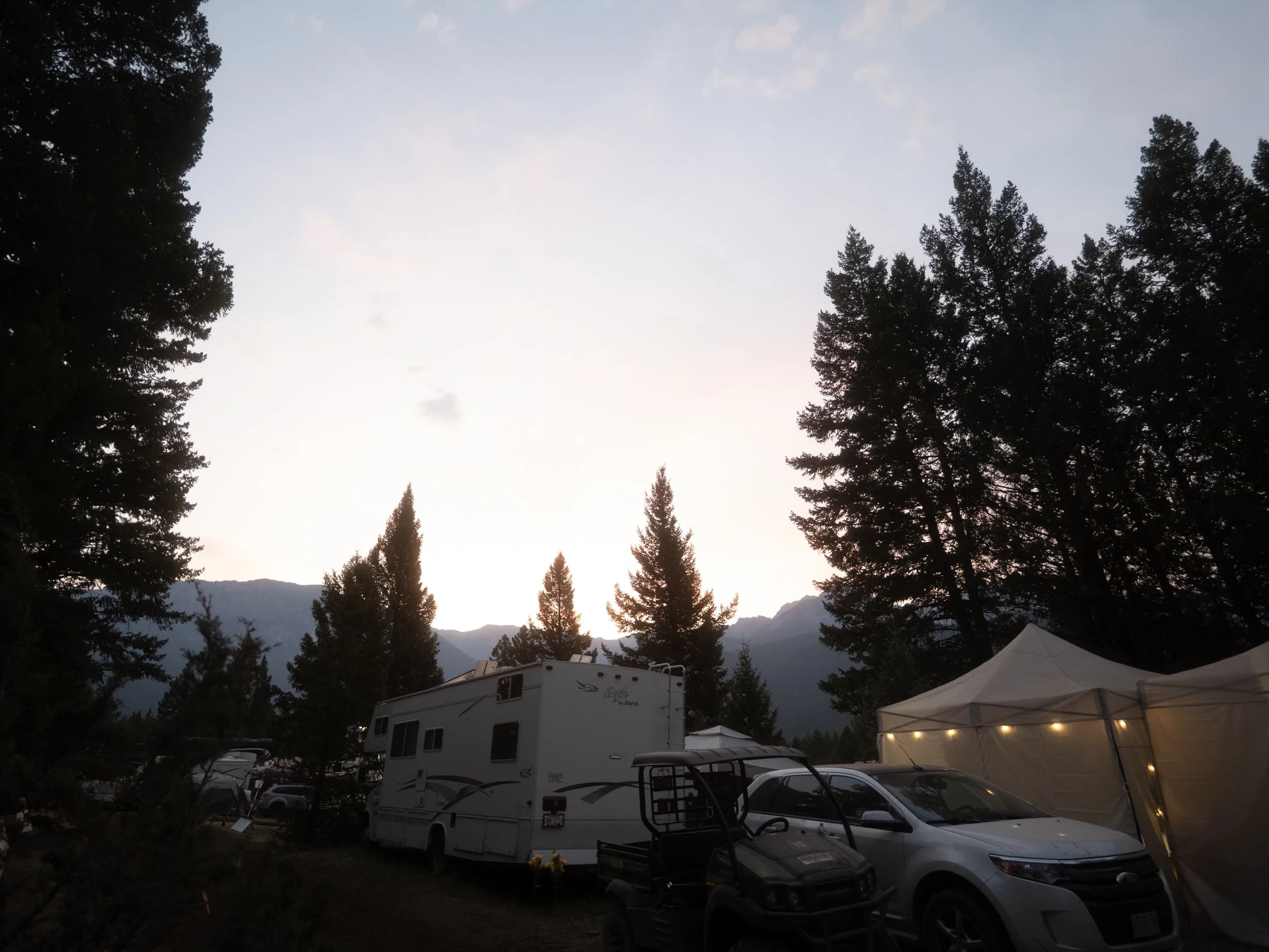 Black-and-white mountain festival grounds with tents and tree line